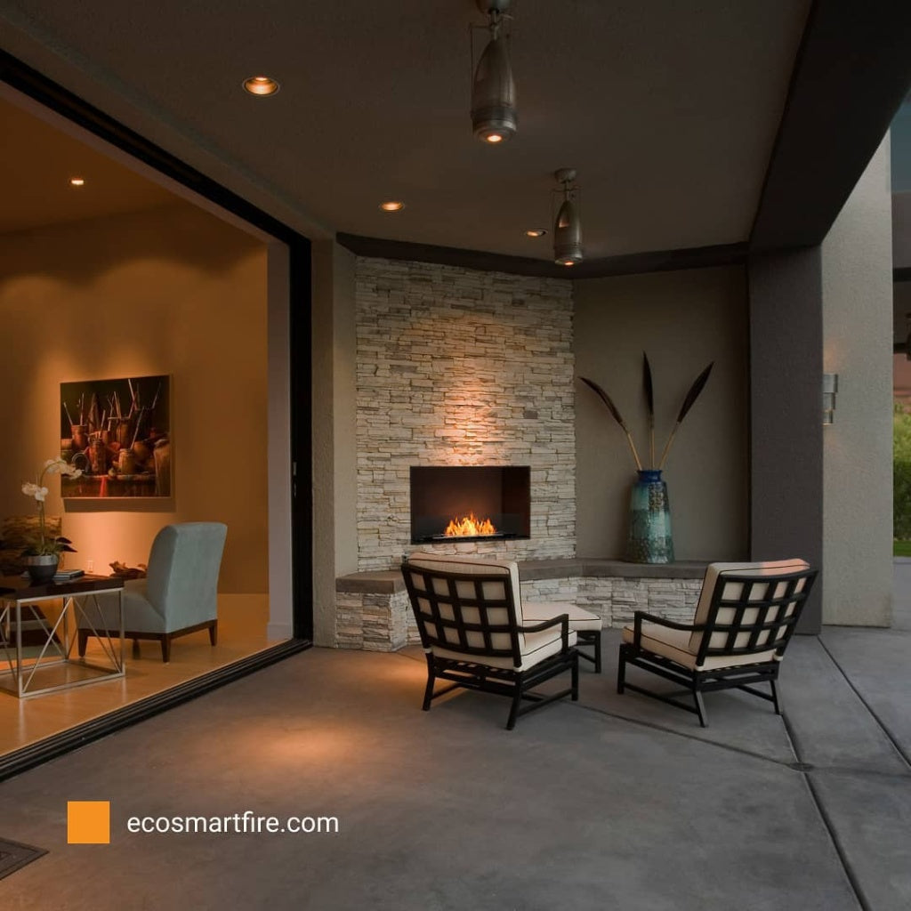 EcoSmart Fire Grate 30 fireplace insert set in a stone wall on a modern outdoor patio with two lounge chairs.