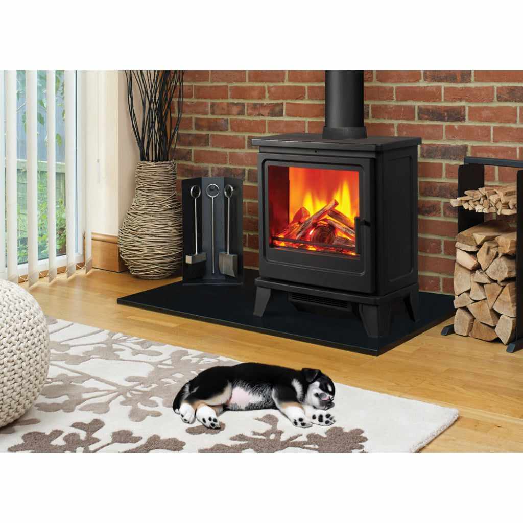 Solution Fires Blackthorn Electric Stove in black with a glowing log flame effect, set on a hearth before a brick wall.
