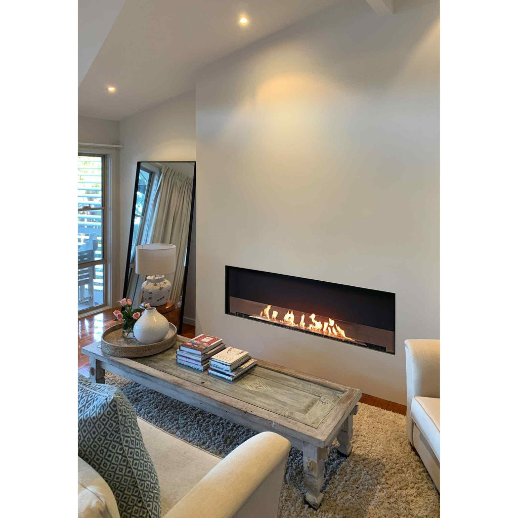 EcoSmart Fire Flex 68 bioethanol fireplace recessed in a white wall above a rustic wooden coffee table in a living room.
