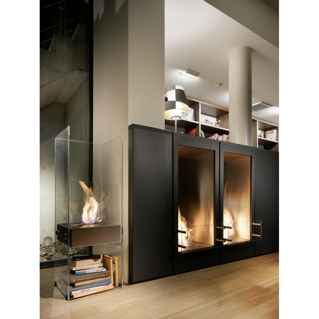 EcoSmart Fire Ghost bioethanol fireplace with glass panels and a stack of books, next to two built-in black fireplaces.