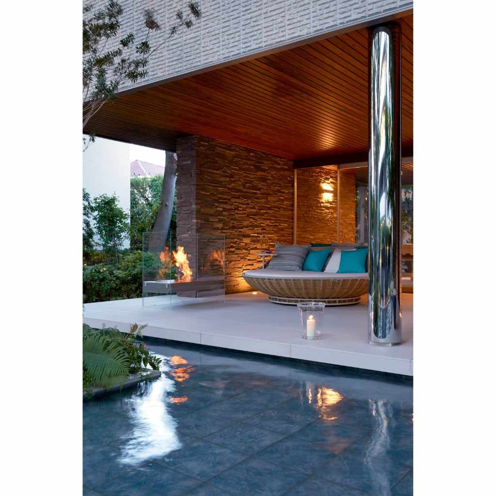 EcoSmart Fire Igloo bioethanol fireplace with glass sides burning on a modern patio beside a pool and lounge area.