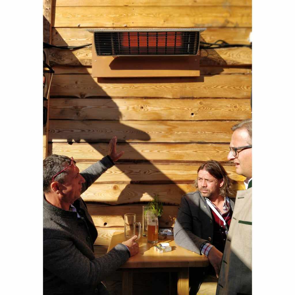 Heatscope Heaters Spot 1600W electric radiant heater mounted on a wooden wall above three men sitting at a table.