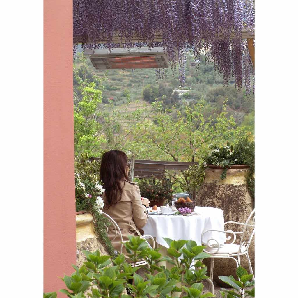Heatscope Heaters Spot 1600W electric radiant heater mounted above a woman dining on a scenic outdoor terrace.