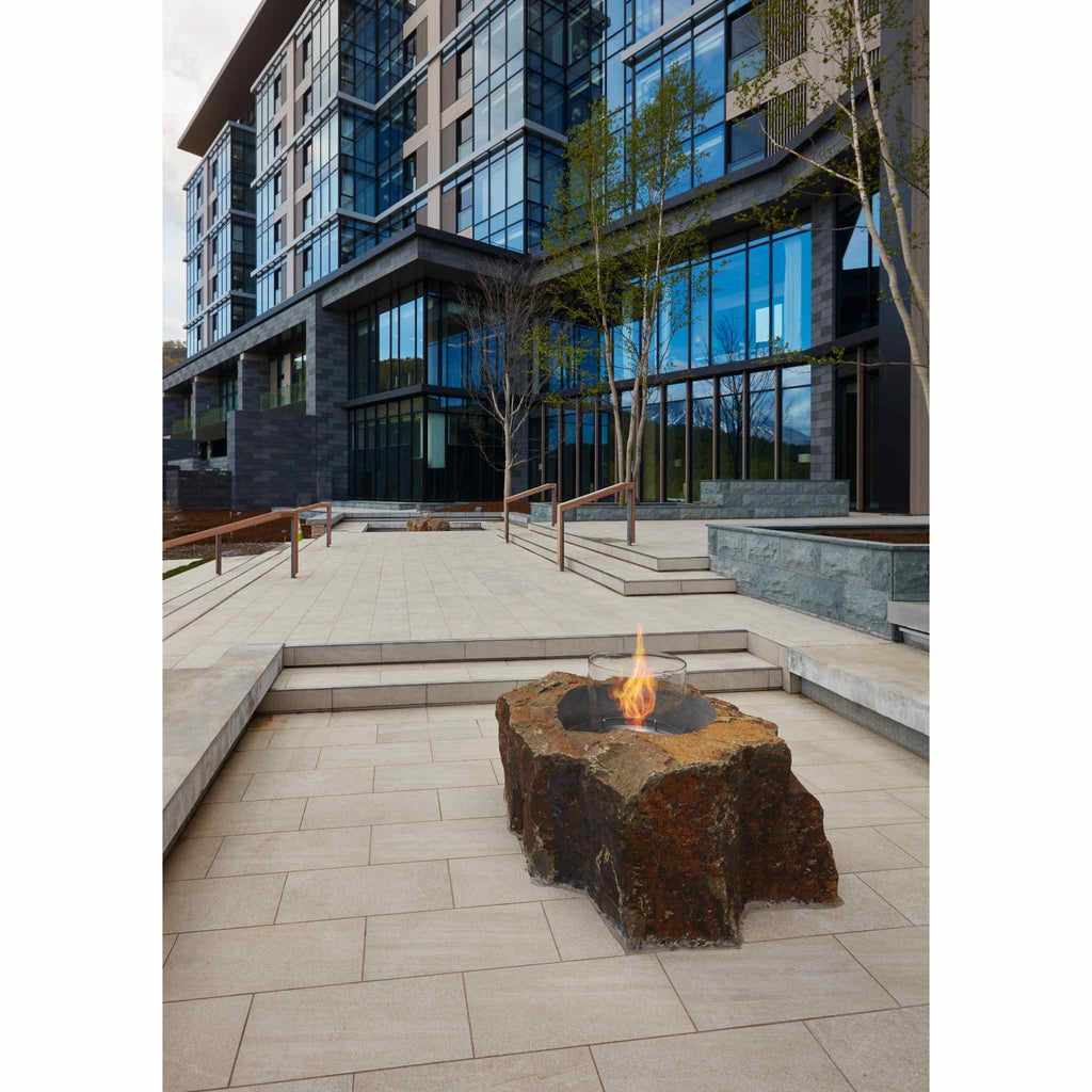 EcoSmart Fire AB8 ethanol burner set in a natural, rugged stone base with a glass screen on a paved outdoor terrace.