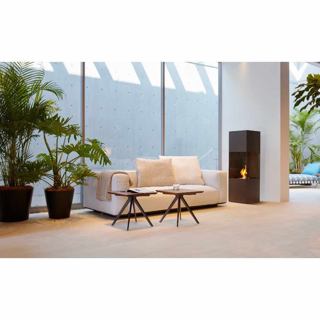 EcoSmart Fire BE bioethanol fireplace in a tall, black metal design with a visible flame in a modern living room.
