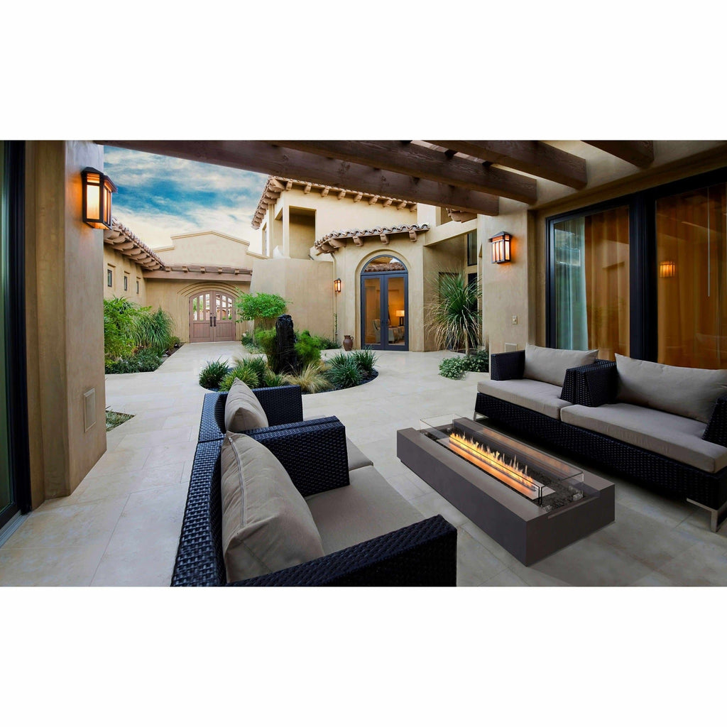 EcoSmart Fire Cosmo 50 bioethanol fire pit table with a grey rectangular base on a stone patio with outdoor sofas.