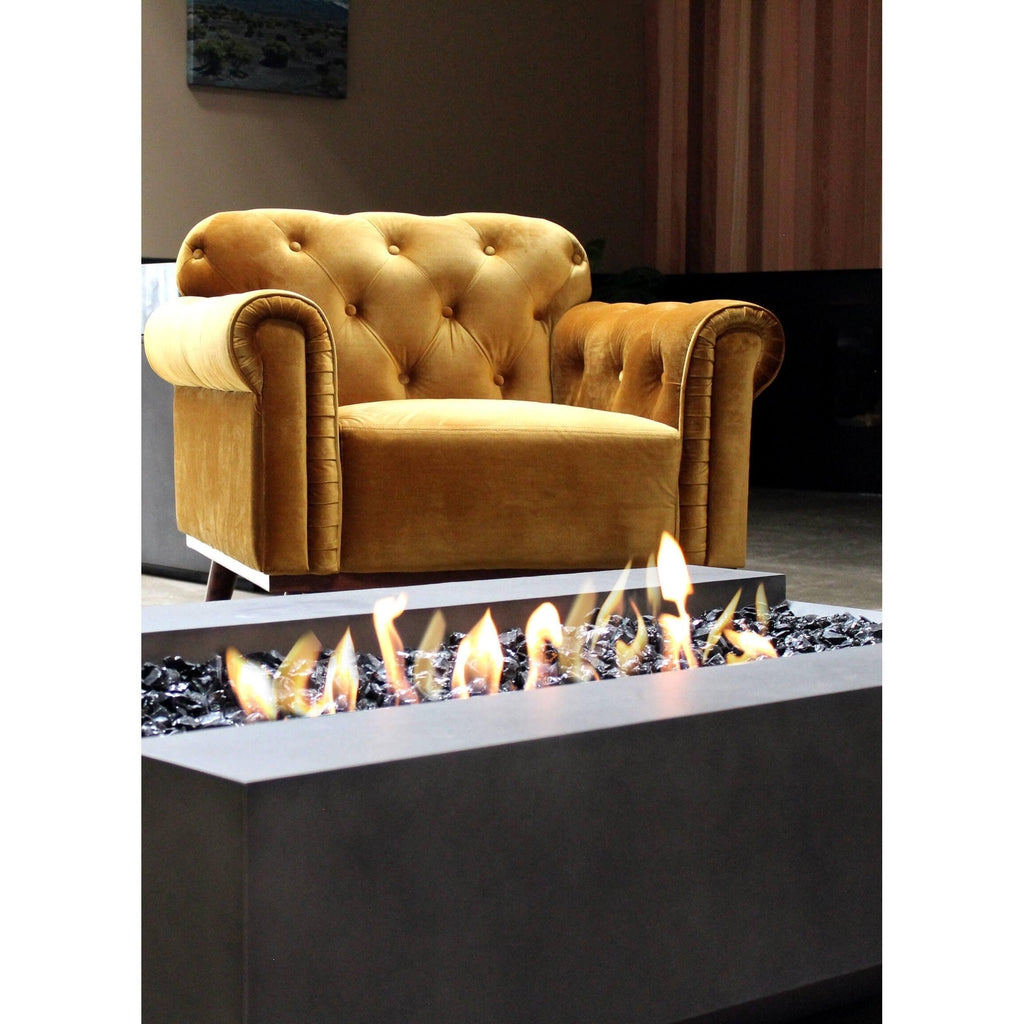EcoSmart Fire Cosmo 50 bioethanol fire pit with black glass media and flames, set before a mustard velvet armchair.
