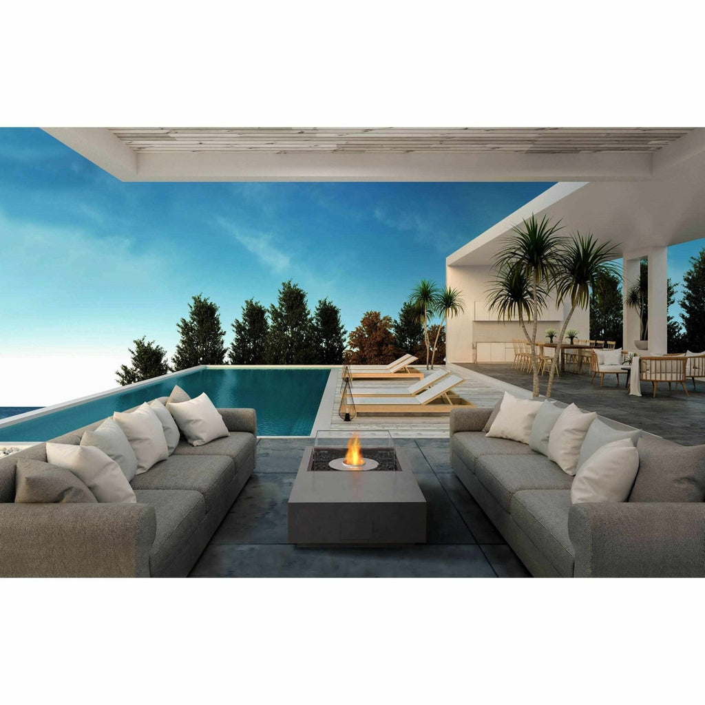 EcoSmart Fire Manhattan 50 bioethanol fire pit table between grey sofas on a modern patio by an infinity pool.