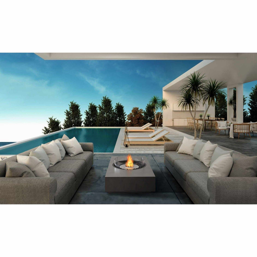 EcoSmart Fire Martini 50 bioethanol fire pit table in grey, positioned between two outdoor sofas by a swimming pool.