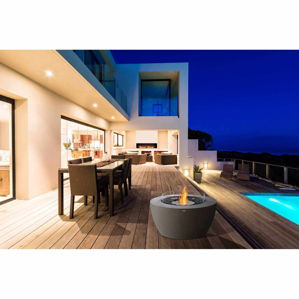 EcoSmart Fire Pod 40 bioethanol fire pit bowl in grey concrete on a modern wooden deck beside a swimming pool at night.