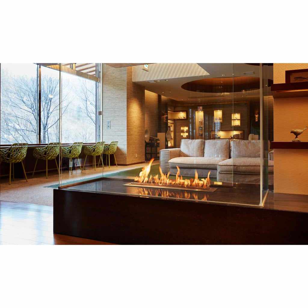 EcoSmart Fire XL700 ethanol burner with a linear flame set in a dark, glass-enclosed fireplace in a modern lounge.