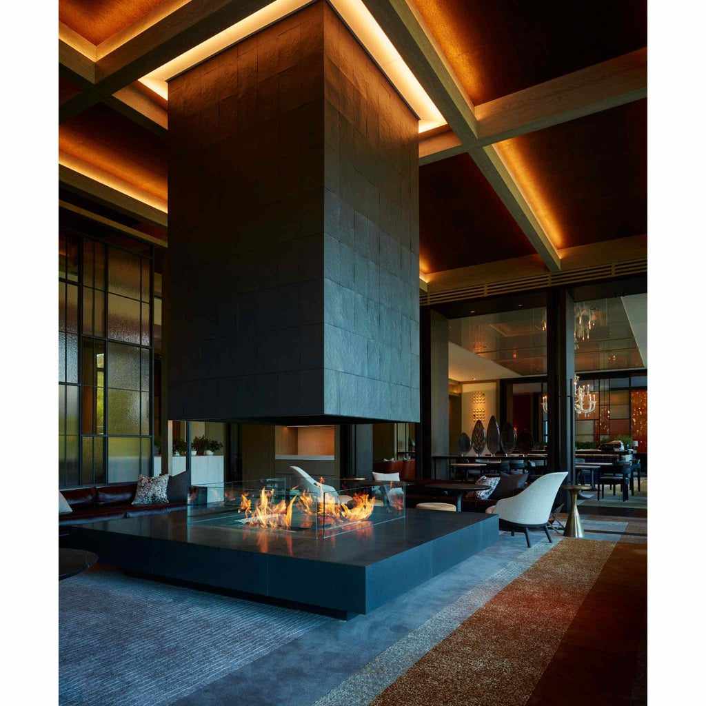 EcoSmart Fire XL700 ethanol burner set in a large, black stone central fireplace with a glass surround in a lounge.