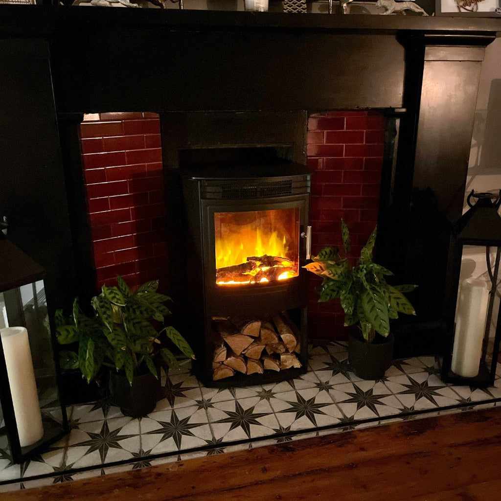 Flametek Alto T electric stove with glowing log effect, set against a dark red tiled fireplace and patterned floor.