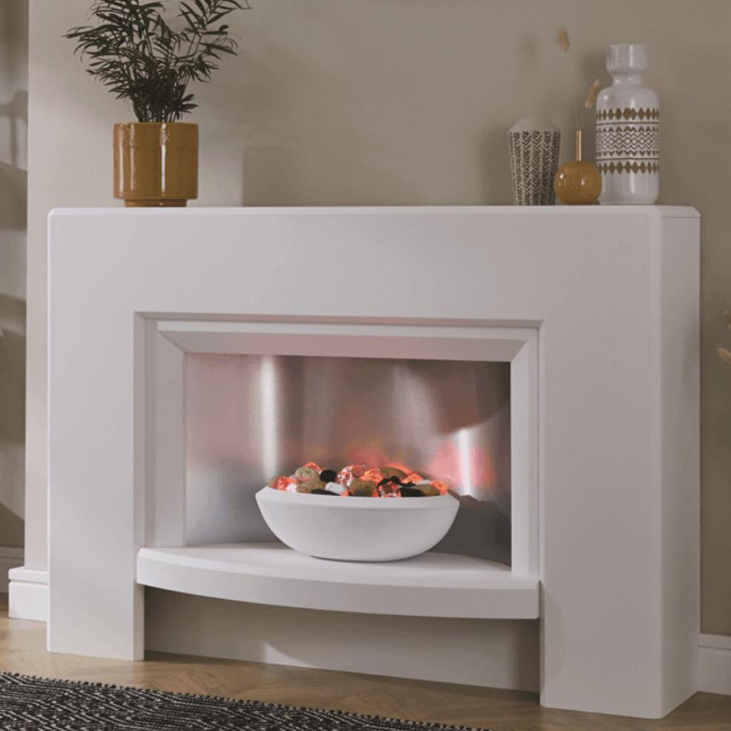 Suncrest Stockeld Electric Fireplace Suite in white with a curved hearth, silver back panel, and glowing pebble fuel bed.